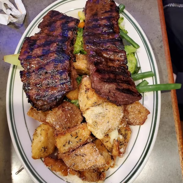 Grilled steak with crispy seasoned potato wedges and green beans on a white plate.