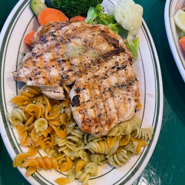 Grilled chicken breast with pasta, broccoli, carrots, and cauliflower on a white plate.